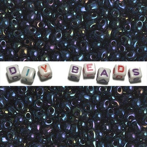 May include: A large quantity of dark blue iridescent seed beads. The beads are small and round with a hole in the center. The beads are arranged in a random pattern. The word "DIY BEADS" is spelled out in white letters on a white background.