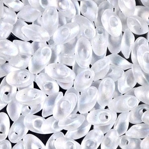 May include: A close-up of a pile of white oval seed beads with a slight iridescent sheen.