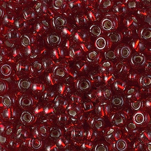 May include: A close-up image of a pile of small, round, red glass beads. The beads have a shiny, iridescent finish.