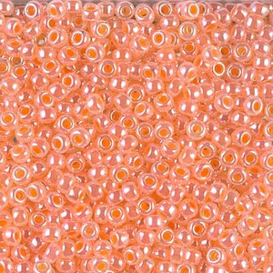 May include: A close-up view of a large quantity of small, round, peach-colored glass beads. The beads have a slight iridescent sheen and are perfect for jewelry making.