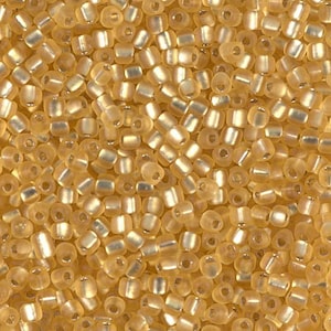 May include: A close-up image of a large quantity of small, opaque, light gold seed beads. The beads have a slightly iridescent finish.