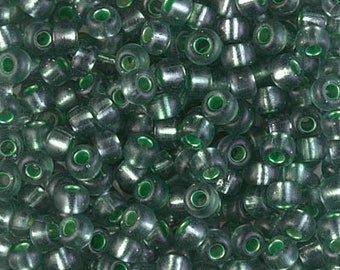 May include: A close-up image of a large quantity of small, round, green glass beads. The beads have a slightly iridescent finish.