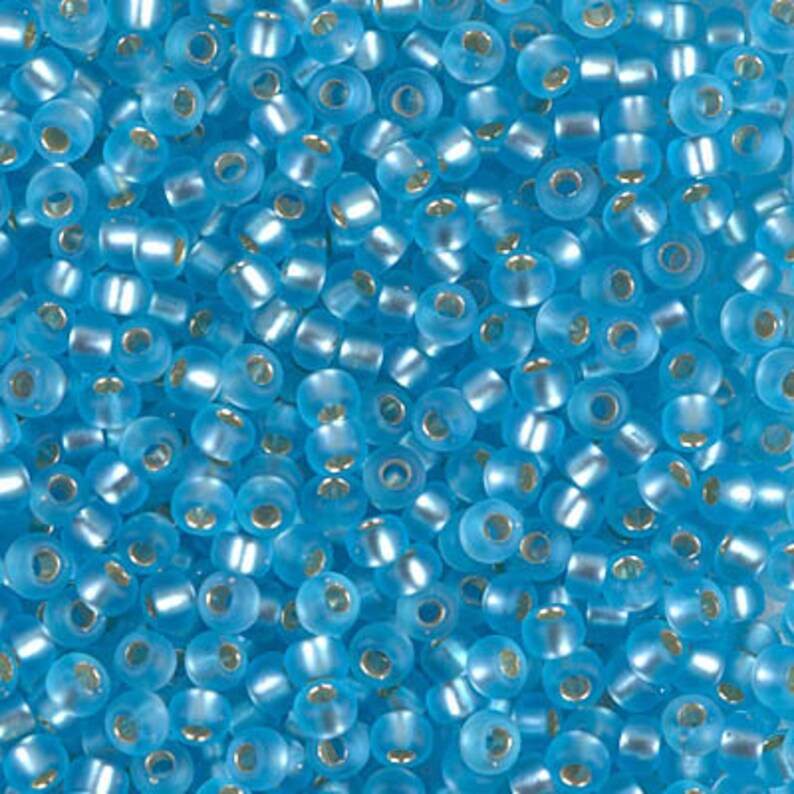 May include: A close-up view of a large quantity of small, round, light blue glass beads. The beads have a slightly iridescent finish.