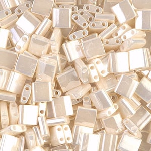 May include: A close-up of a pile of small, square, iridescent, off-white glass beads. The beads have a subtle shimmer and are perfect for jewelry making or other craft projects.