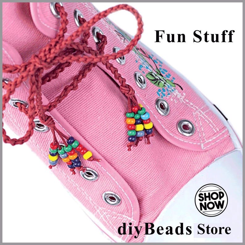 May include: A pink canvas sneaker featuring dark red braided laces adorned with multi-colored beads at the ends. The shoe includes silver metal eyelets and white stitching. Text on the image reads Fun Stuff and SHOP NOW diyBeads Store.