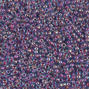 Puede incluir: Una vista de cerca de una gran cantidad de pequeñas cuentas de vidrio redondas e iridiscentes. Las cuentas son una mezcla de colores púrpura y azul con un brillo metálico.