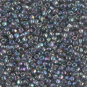 May include: A close-up view of a pile of small, iridescent seed beads. The beads are primarily a dark gray color with a shimmering, rainbow-like sheen. The beads are cylindrical with a hole running through the center, perfect for stringing.
