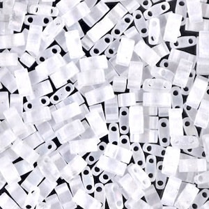 May include: A close-up view of a large quantity of small, white, opaque, rectangular seed beads. The beads have two holes on each side.