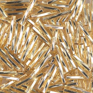 May include: A large pile of gold glass beads in the shape of long, thin cylinders. The beads are shiny and reflective, and they are all mixed together in a random pattern.