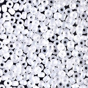May include: A close-up view of a large quantity of small, white, opaque seed beads. The beads are round with a hole in the center.
