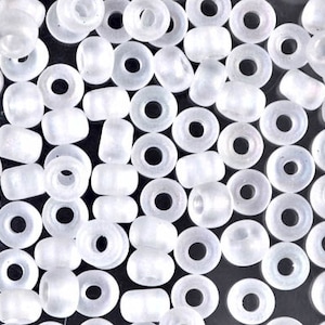 May include: A close-up of a pile of white opaque seed beads. The beads are round and have a hole in the center.
