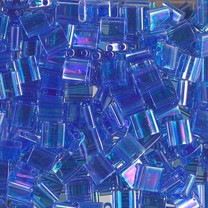May include: A bulk pack of iridescent blue glass seed beads. The beads are small and square shaped with a hole in the center.