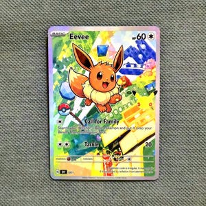 Könnte beinhalten: Eine holografische Eevee-Sammelkarte mit dem Charakter in der Mitte vor einem bunten, abstrakten Hintergrund. Die Karte zeigt den Text Eevee, HP 60, Call for Family und Tackle sowie eine kleine Pikachu-Illustration und ein Pokéball-Symbol.