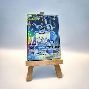 May include: A Squirtle Squad GX Tag Team trading card featuring a blue armored character with cannons, displayed on a small wooden easel. The card has a holographic finish, 200 HP, and lists attacks Mega Stomp and Hydro Pump Squad Style.
