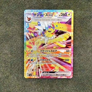 Op de afbeelding: Een holografische Jolteon ex ruilkaart met een geel wezen met stekelig wit bont, kleurrijke kristallen accenten en Japanse tekst. De kaart toont 260 HP, een bliksemenergiesymbool en de aanvalsnamen Flash Spear en Tera Bite.