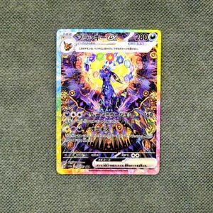 Può includere: Una carta collezionabile olografica Umbreon ex raffigurante una creatura viola scuro con anelli gialli, circondata da uno sfondo cristallino vibrante e multicolore con gemme fluttuanti. La carta mostra testo in giapponese e 280 HP.