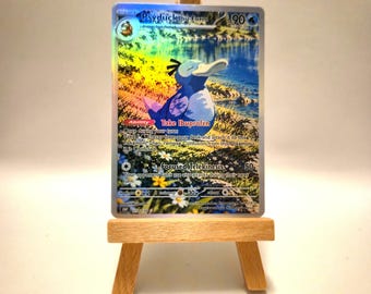 May include: A holographic trading card featuring a blue Psyduck character with the text Psyduck Ibu-Form and Take Ibuprofen, displayed on a small wooden easel. The card shows a lakeside scene with yellow and white flowers in the foreground.