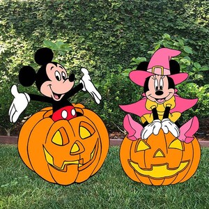 May include: Two Halloween-themed yard decorations featuring Mickey Mouse and Minnie Mouse. Mickey is emerging from an orange jack-o'-lantern. Minnie Mouse is wearing a witch hat and cape, sitting on a pumpkin.