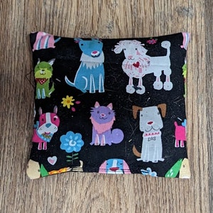 May include: A black fabric pouch with a colorful pattern of dogs and cats. The pouch is filled with small objects, such as beans or rice, to create a weighted sensory toy.