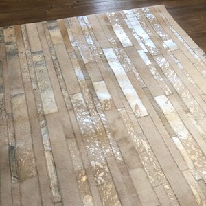 May include: A white and silver cowhide rug with a geometric pattern. The rug is made of strips of leather that are sewn together to create a unique design.