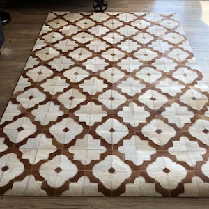 May include: A white and brown cowhide rug with a geometric pattern. The rug is made of leather and has a natural, rustic look.