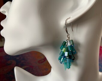 May include: Teal and green glass bead dangle earrings with silver hooks. The earrings are cascading and have a teardrop shape.