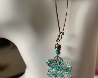 May include: A pair of turquoise blue dangle earrings with a delicate flower design and a small bead accent. The earrings are made of metal and have a vintage look.