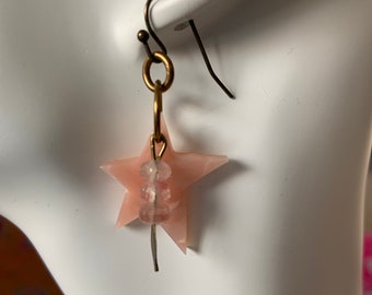 May include: Pink star-shaped earrings with a gold hook and clear beads hanging from the star.