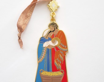 May include: Gold-toned Christmas ornament depicting the Holy Family. Mary, Joseph, and baby Jesus are shown in a traditional style with colourful clothing. The ornament has a brown ribbon for hanging.