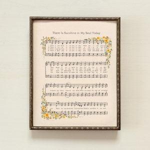 May include: A vintage sheet music print with a gold frame. The sheet music is for the song "There Is Sunshine in My Soul Today". The lyrics and musical notes are printed in black ink on a cream-colored background. The sheet music is decorated with yellow and green floral illustrations.