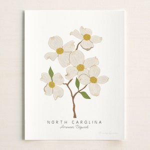 Puede incluir: Una impresi&oacute;n de flores de Cornus florida blancas y amarillas con el texto "NORTH CAROLINA" y "American Dogwood" en marr&oacute;n.