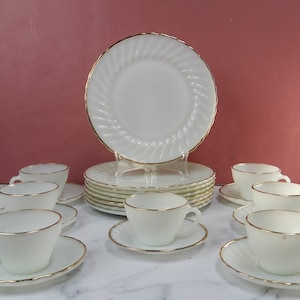May include: A set of white milk glass dinnerware with a gold trim. The set includes cups, saucers, and dinner plates.
