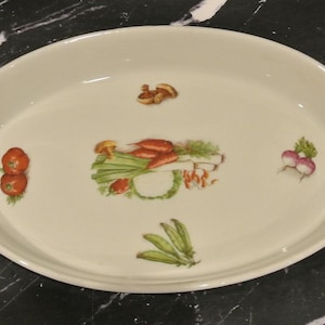 May include: An oval-shaped white ceramic serving dish featuring a central illustration of assorted vegetables including carrots, leeks, and greens, surrounded by smaller individual depictions of red tomatoes, radishes, peas, and a single mushroom.