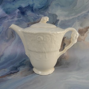 Puede incluir: Tetera de cerámica blanca con un diseño de rosas y una tapa en forma de rosa. La tetera tiene un asa y un pico.