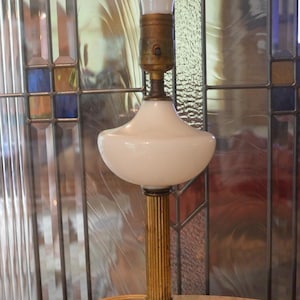 May include: A table lamp featuring a square white marble base, a vertical fluted brass column, and a smooth white glass shade. The lamp includes a brass socket and a clear light bulb at the top, with a coiled beige electrical cord extending from the base.