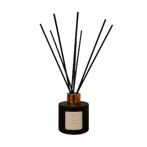 May include: A black reed diffuser with a copper-coloured collar and black reeds. The diffuser has a white label with text. The product is designed to release fragrance into a room. The overall aesthetic is modern and minimalist.