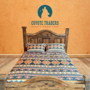 May include: Rustic wooden bed frame with a patterned quilt and two matching pillows. The quilt features a geometric design in shades of blue, orange, and white. The headboard has a curved top. The logo for Coyote Traders Rustic Furniture is visible.