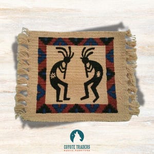 May include: Beige woven square with a Kokopelli design in black. The border features a geometric pattern in red, blue, and black. The edges have a fringe. The Coyote Traders logo is at the bottom.