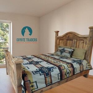 May include: A rustic wooden bed frame with a headboard and footboard. The bed is covered with a patterned blanket in shades of cream, brown, and navy. Two pillows are on the bed. The wall features the text "COYOTE TRADERS RUSTIC FURNITURE".