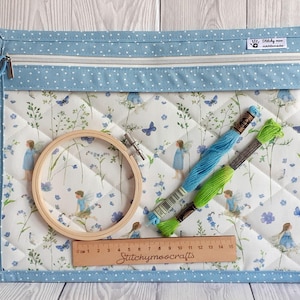 Könnte beinhalten: Eine blau-weiß gesteppte Bastel-Organizer-Tasche mit Reißverschluss, Pünktchen-Besatz und einem Blumen- und Feenmuster. Enthält einen hölzernen Stickrahmen, Faden und ein Lineal mit dem Text "Stitchymoo crafts".