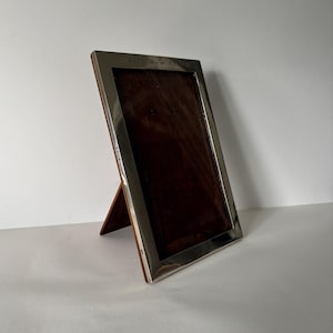 May include: A silver-plated picture frame with a wooden backing. The frame is engraved with the text "A.T.C. New York".