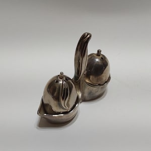 May include: Silver salt and pepper shakers shaped like pears with a leaf design. The shakers are attached to a silver base.