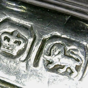 May include: Close-up of a silver hallmark with a crown and a lion. The crown is above the lion, which is facing right. The hallmark is on a piece of metal.