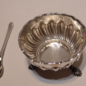 Puede incluir: Un salero de plata con un interior acanalado y tres patas. Viene con una cuchara de plata a juego.