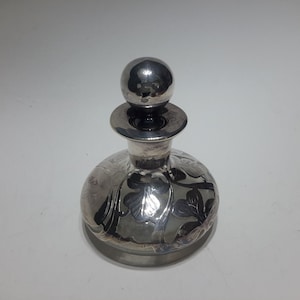 May include: A silver and glass perfume bottle with a round stopper and an etched floral design.