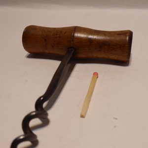 Può includere: Un cavatappi vintage con manico in legno e spirale in metallo. Il cavatappi è grande circa come un fiammifero.