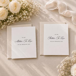 May include: Two white greeting cards with envelopes, each featuring black printed text. One card reads To My Mother-In-Law On My Wedding Day, and the other reads To My Father-In-Law On My Wedding Day. The cards are surrounded by white roses and baby's breath.