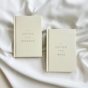 May include: Two cream-colored hardcover books with a fabric-like texture. The left book features the text A LETTER TO MY HUSBAND in dark brown lettering. The right book features the text A LETTER TO MY WIFE in dark brown lettering.