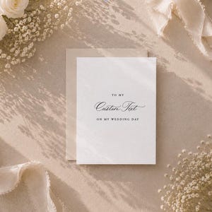 May include: A white rectangular greeting card with a matching envelope featuring the black printed text TO MY Custom Text ON MY WEDDING DAY. The card is surrounded by white roses and baby's breath flowers with a flowing light beige fabric ribbon.