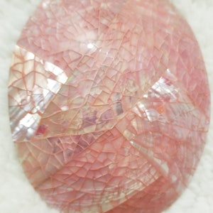 May include: A pink oval-shaped decorative object made of small, iridescent, mosaic-like pieces of shell.